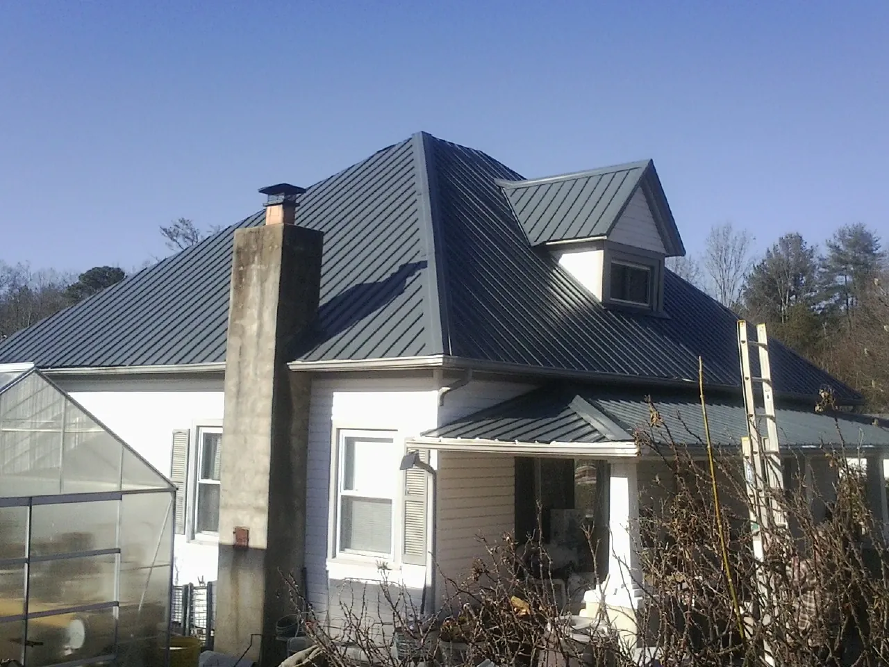 Dark blue standing seam metal roof on a white farmhouse with dormer — Slate & Tile Roof Repair by Roofing Brothers in Decker